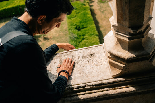 Person Leans Over a Balcony Looking at a Garden Below in the Afternoon