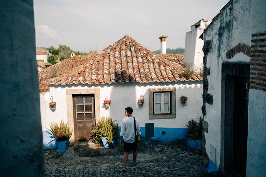 Person Walks Outside a Blue and White House in a Cobblestone Street