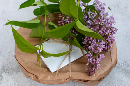 Handmade parcel tied with twine string on grey concrete background, rustic greeting card mockup with blooming flower