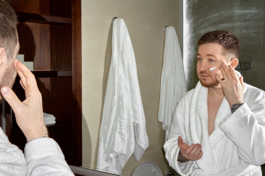 Man applying face cream in bathroom mirror