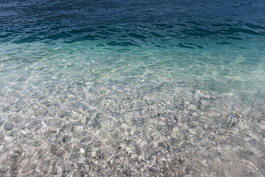A refreshing view of shallow, pristine water with rippling waves and a clear view of the stony substrate beneath the surface.