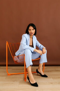 Woman in light blue suit sitting on orange chair