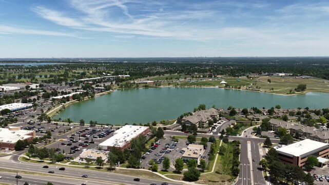 Aerial of suburban lake and commercial development at Clement Park in Colorado with residential neighborhoods strip malls and parking lots in summer