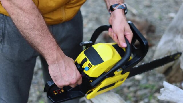 Slow motion 4K footage of a hands of a man starts his chainsaw and begins cutting down a tree felled by the hurricane. Close-up of hands and a chainsaw.