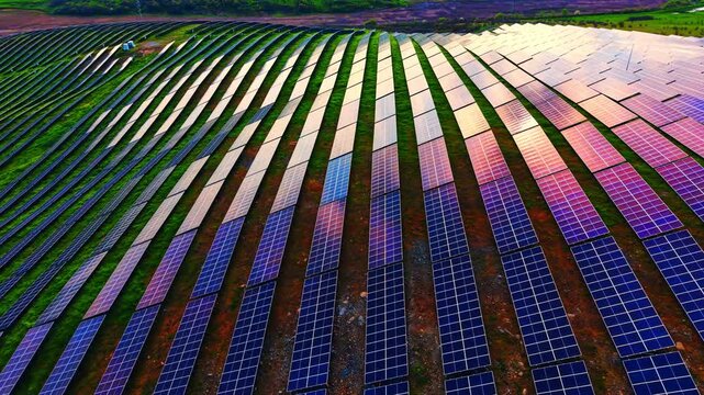 Vast array of colorful photovoltaic modules on a slope, viewed from a high overhead angle with parallel lines displaying purple and blue reflections.