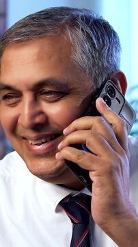Indian executive working on computer while attending phone call at desk in modern office, Asian corporate professional multitasking with focus and communication skills in contemporary workplace setup
