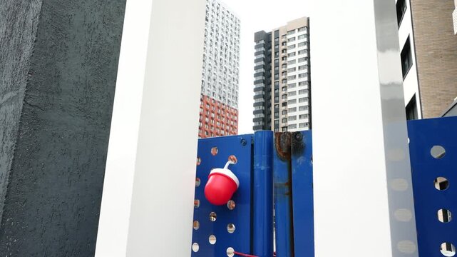 Close-up of construction site gate with emergency stop button and modern urban buildings in background