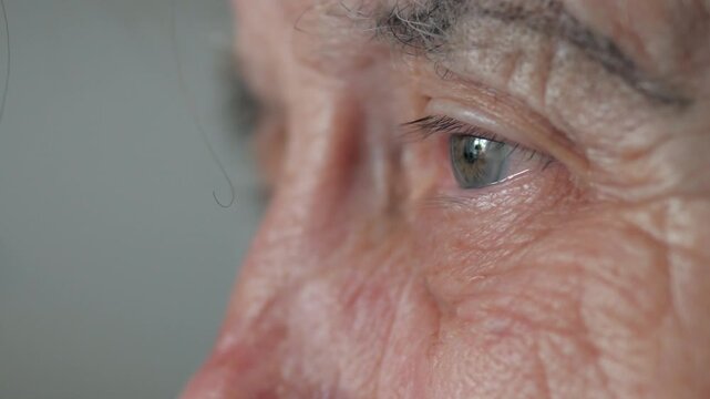 Extreme close up elder woman blue eye, showing detailed wrinkles and weathered skin, reflecting lifetime of wisdom memory and experience. Old female suffers from tremor and nervous tic of head shaking