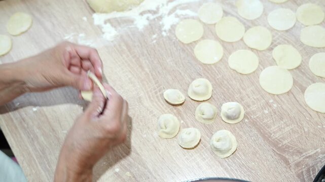 Woman preparing traditional homemade dumplings by hand on kitchen table with dough circles and filling ingredients