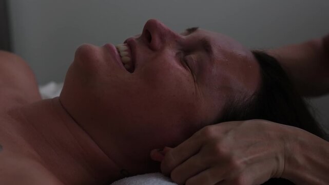 A professional close-up slow-motion video of a wellness facial massage treatment. A professional female masseuse gently and delicately massaging the glowing skin of a young woman's face at a luxury sp