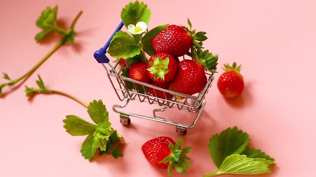 strawberries in small grocery cart on light pink background