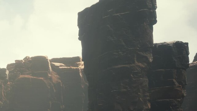 Tall rock formations rise against the sky. Sunlight hits the jagged edges, creating shadows. The canyon stretches into the distance showing rugged terrain and steep cliffs.