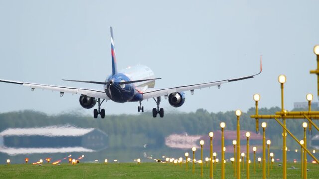 Commercial Airplane Landing Gear Deployed Approaching Runway with Airport Lights and Grass Field