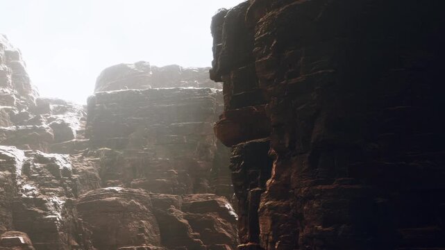 A view of a rocky landscape during daylight. Sunlight highlights the textures of the cliffs. The scene shows shadows and light interacting on the surfaces of the rocks.