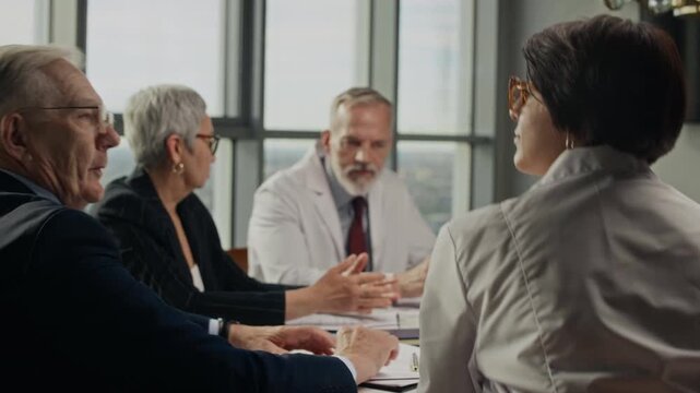 Zoom out shot of senior Caucasian businessman standing up and shaking hands with female scientist during corporate meeting. Clip is ideal for energy sector and business partnership videos