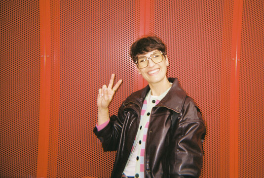 Smiling woman making peace sign against red background