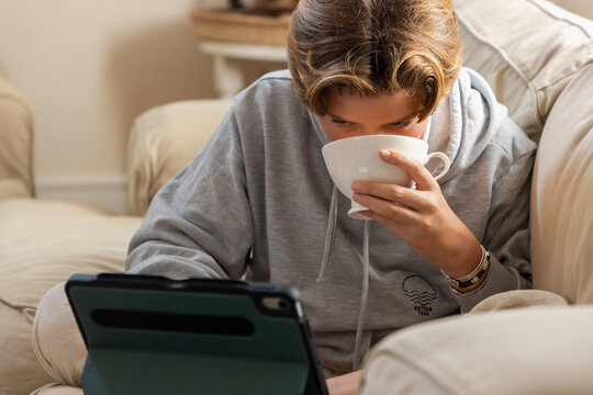 pre teen boy on sofa sipping tea and watching tablet