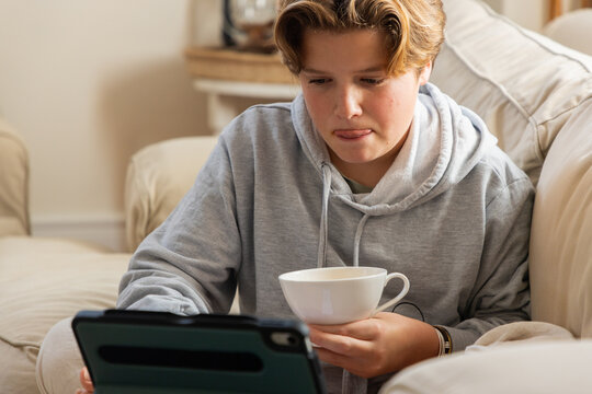 pre teen boy on sofa sipping tea and watching tablet