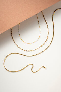 Layered Gold Chain Necklaces on Minimalist  Peach and White Background