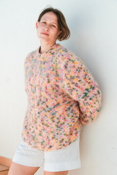 Young Woman Leans Against Wall Wearing Colorful Sweater and Shorts