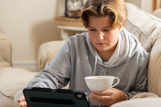 pre teen boy on sofa sipping tea and watching tablet