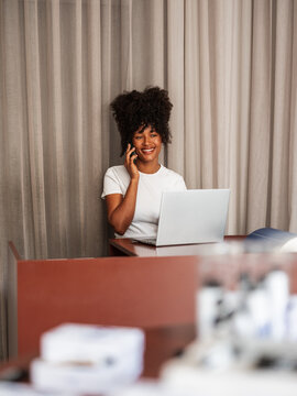 Smiling Receptionist Talking On Phone While Working At Laptop 