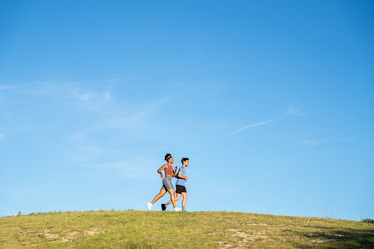 Couple running on grass hill under clear sky