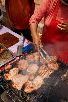 Street vendor grills chicken in a busy market in the afternoon