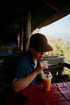 Traveler drinks Thai tea on deck with view of mountains in daytime