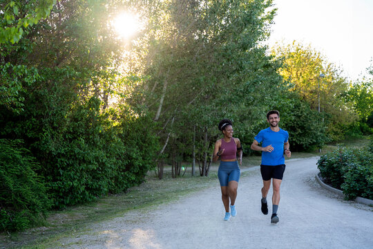 Diverse couple running together on sunny park path