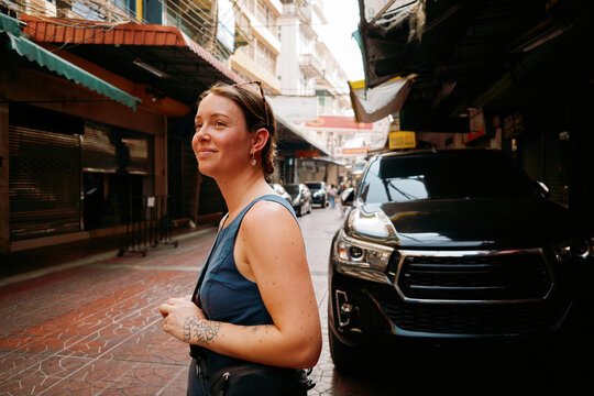 Woman walks in a quiet street in Bangkok. She's taking in the sights. 