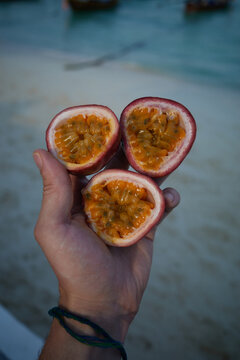 Holding fresh passion fruit by a beach with boats in the background