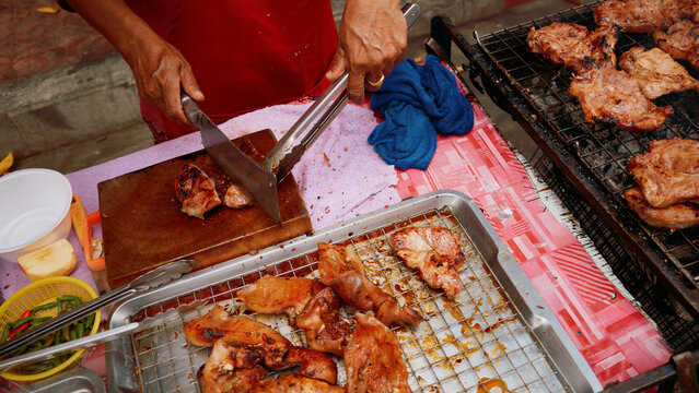 Street vendor grills chicken in a busy market in the afternoon