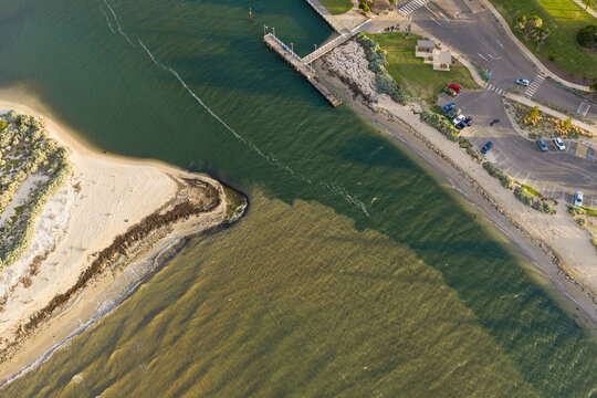 Coastal river mouth flowing past a sandy point and shoreline carpark