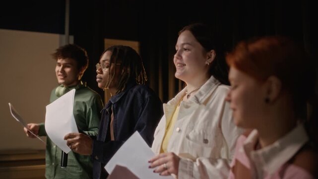 Medium shot of diverse teenagers holding scripts and rehearsing theater performance on stage. Clip for marketing high school drama clubs, extracurricular activities, and creative arts education