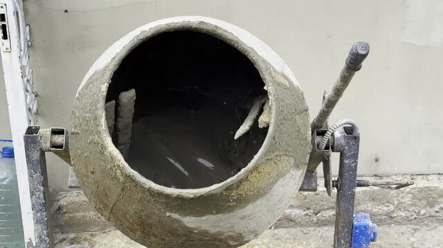 Close up of concrete being mixed inside a cement mixer. The rotating drum blends the materials together, creating smooth and consistent mixture prepared for construction work on building site