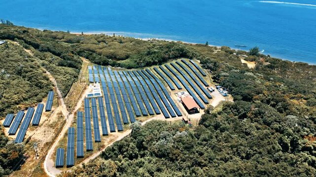 Aerial view of a large solar panel array surrounded by lush tropical forest along the blue coastline of Guanaja, Bay Islands Department, Honduras.