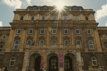 Fototapeta premium ​Horizontal low angle view of a grand historic palace facade with symmetric windows. Majestic classical architecture under a bright sun flare, shot in Budapest, Hungary