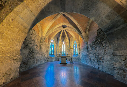 ​Horizontal wide angle view of an ancient underground stone crypt with an altar. Historic medieval chapel interior under a gothic brick vaulted ceiling, shot in Budapest, Hungary