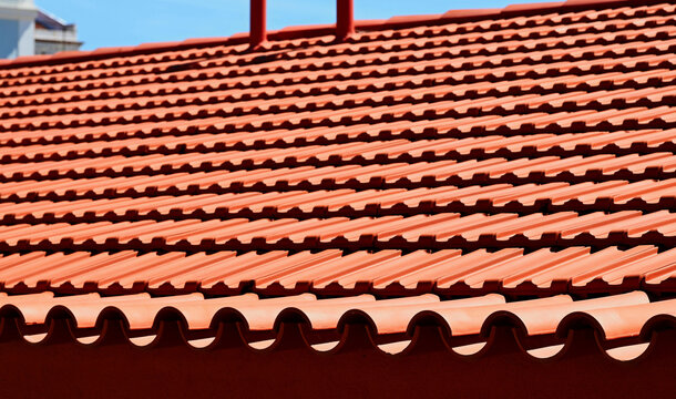 sloped residential clay tile roof. red brown tiles under blue sky. bright color roof tiles and roof ridge under beautiful fresh white cumulus clouds in bright sunlight. construction material concept