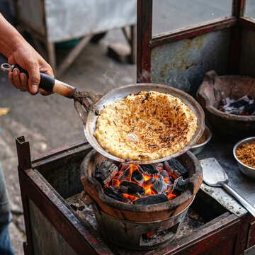 Cooking Kerak Telor, Indonesian Traditional Spicy Omelette Street Food from Jakarta, Chef Hand Flipping Sticky Rice on Small Frying Pan over Burning Charcoal Clay Stove, Food Photo