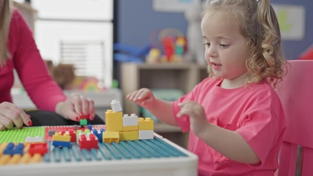Little girl stacking yellow and white plastic blocks with fingers at a play table in a building; concentration learning.