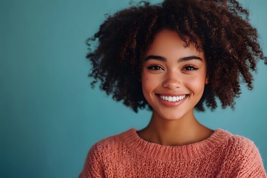 Portrait of a beautiful african american woman with curly hair, smiling genuinely against a vibrant teal background.