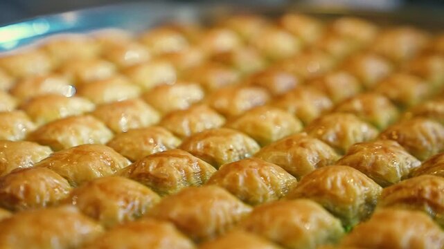 Close up shot of golden Turkish baklava inside a round metal baking tray. Macro details of crispy pastry layers soaked in sweet syrup.