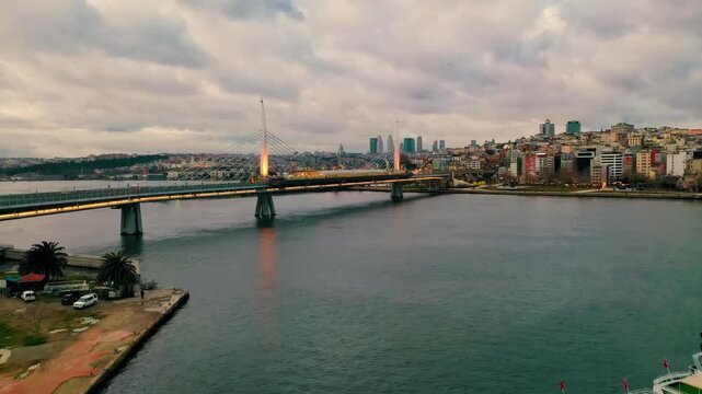Aerial drone shot of Halic Metro Bridge in Istanbul. Golden Horn panoramic view with modern architectural landmarks and sea reflection at sunset.