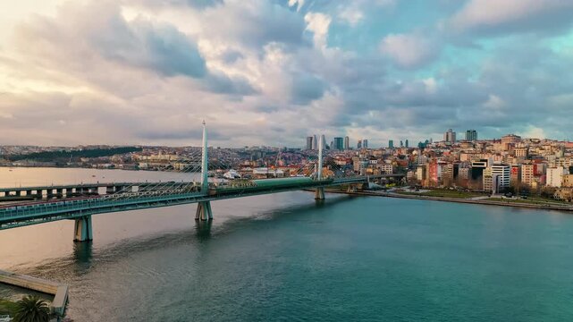 Aerial drone shot of Halic Metro Bridge in Istanbul. Golden Horn panoramic view with modern architectural landmarks and sea reflection at sunset.