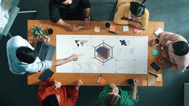 Diverse Team Engaging in Collaborative Meeting to Analyze Data and Create Strategic Plans Around a Large Table with Visual Charts and Graphs Gluon.