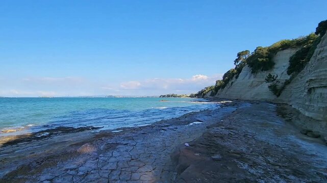 Auckland, New Zealand - Baywater layered coastal cliffs rocky shoreline turquoise ocean clear sky geological landscape nature travel video. Excellent for travel, nature and landscape stock footage. 