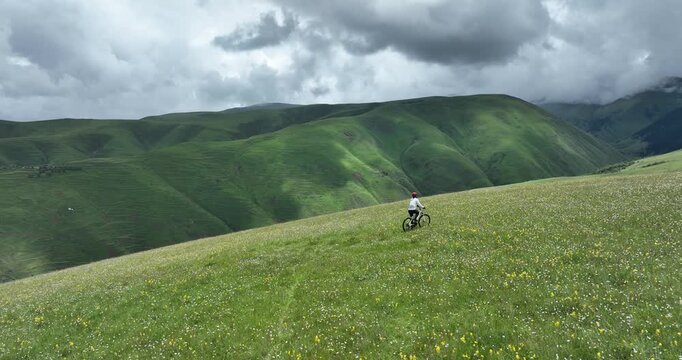 Aerial footage of woman riding mountain bike on beautiful grassland mountain trail, slow motion