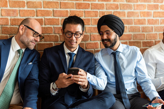 Three men in business attire, sitting and looking at a smartphone.
